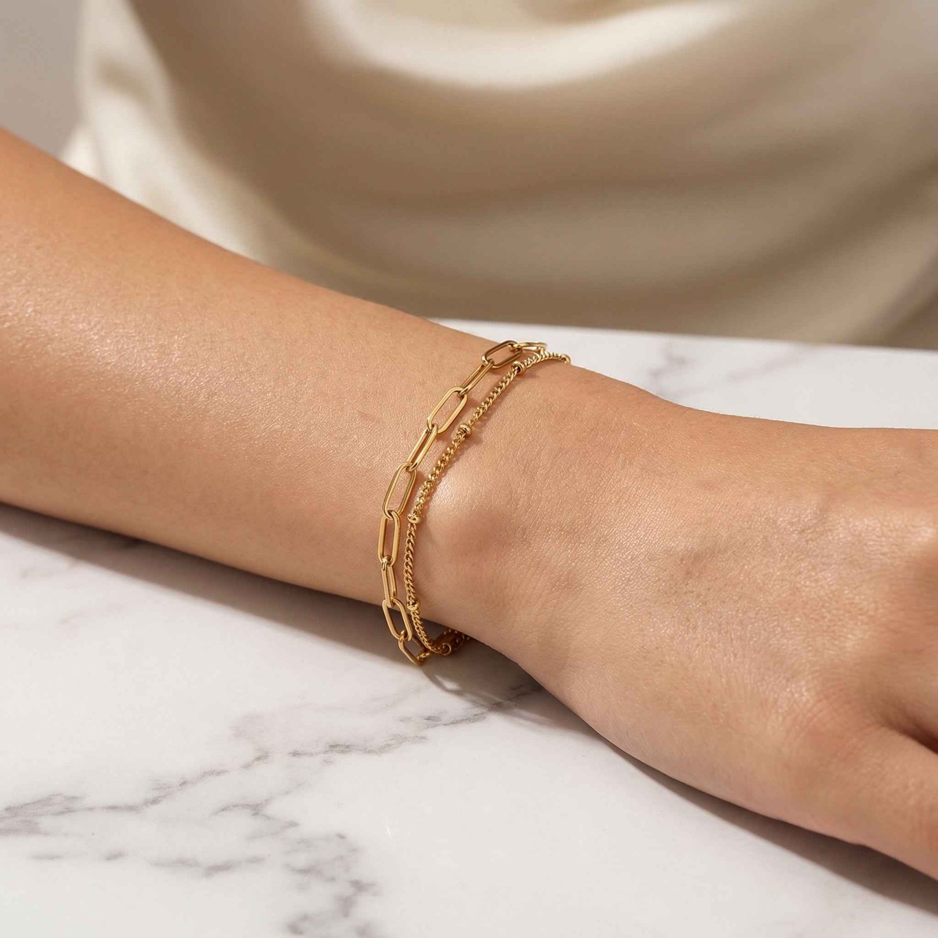 Gold bracelet on a person's wrist with a marble surface background